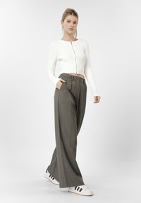 Λευκό ριμπ πλεκτό μακρυμάνικο ζακέτα με φερμουάρ μπροστά, συνδυασμένο με loose fit σκούρο πράσινο παντελόνι με ρίγες και λευκά αθλητικά παπούτσια με μαύρες ρίγες.