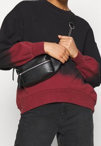 Felpa bloccata nei colori nero e borgogna con scollo rotondo, abbinata a una piccola borsa in pelle nera con chiusura a zip e tracolla a catena.