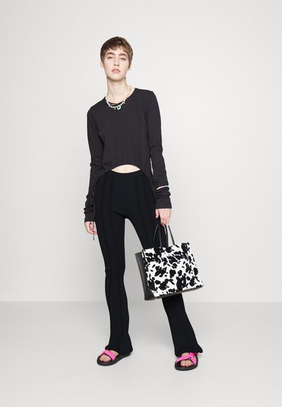 Top preto de mangas compridas, cortado na cintura; calças pretas com textura canelada; sandálias cor-de-rosa; bolsa tote em padrão de vaca preto e branco.