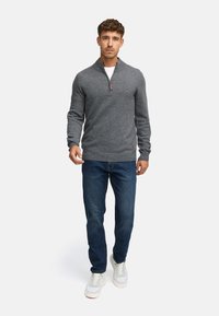 Grå zip-tröja i mjukt material, kombinerad med mörkblå jeans och vita sneakers. Har ribbade ärmslut och en detalj med varumärkeslogotyp.