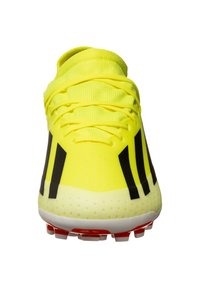Botín de fútbol amarillo brillante con una parte superior texturizada, acentos negros y una suela ligera con tapones rojos para tracción.