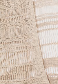 Beige gebreide textiel met een open weefpatroon, featuring afwisselend dikke en dunne strepen, waardoor een gestructureerde uitstraling ontstaat.