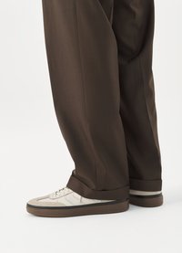 Hvite sneakers med beige semsket skinn-detaljer, med et strukturert mønster og en brun gummisåle, sammen med mørkebrun skreddersydde bukser.