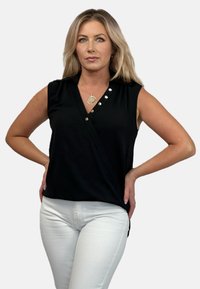 Czarny bezrękawnik z dekoltem w serek, ozdobiony dekoracyjnymi guzikami i asymetrycznym dołem. W zestawie z białymi dopasowanymi spodniami.