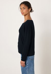 Svart långärmad tröja med avslappnad passform och rund halsringning, kombinerad med höga blå jeans för en avslappnad outfit.