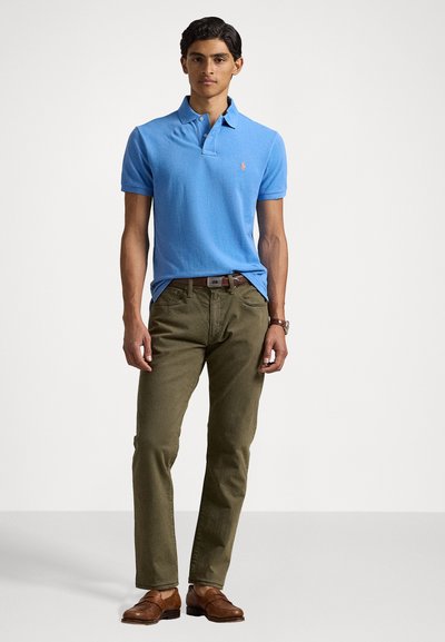 Polo de color azul claro con mangas cortas, combinado con pantalones verde olivo, zapatos de cuero marrón y un cinturón oscuro. Diseño sencillo con un pequeño logo.