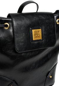 Sac à dos en cuir noir avec un design structuré, quincaillerie dorée et un patch logo carré proéminent. Il dispose d'un rabat supérieur et de poches latérales.