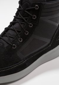 Černé vysoké tenisky s kombinací semišového a síťovaného materiálu, s texturovaným povrchem, černými tkaničkami a šedými gumovými detaily na podrážce.