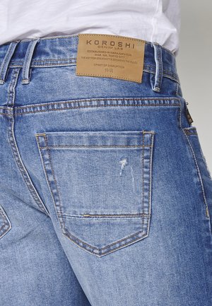 Jeans azzurri chiari con una superficie in denim liscia, design a cinque tasche e un'etichetta in pelle sulla parte posteriore della vita con dettagli del marchio.