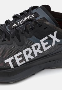 Black and gray athletic shoe with mesh upper, textured design, large white "TERREX" logo, and rubber sole with visible traction patterns.