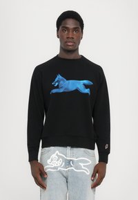 Svart hettegenser med grafikk av en blå løpende rev. Blandingsmateriale av bomull, rund hals, ribbestrikkede mansjetter. Lysevasket denim med hvit rev-design på benet.