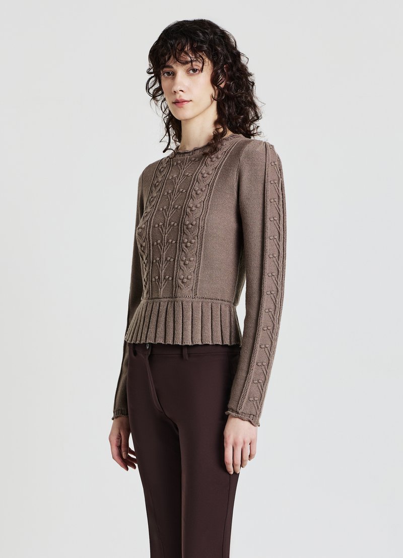 Brauner Strickpullover mit strukturierten Blumenmustern, gerippten Akzenten, einem plissierten Saum und langen Ärmeln, kombiniert mit dunkelbraunen Hosen.
