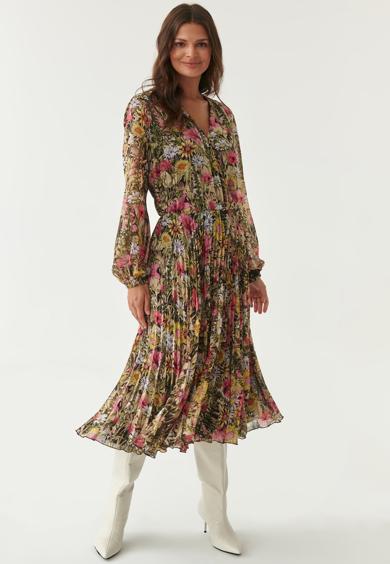 Langes, florales Kleid mit plissiertem Design in lebhaften rosa, gelben und blauen Blumen auf einem grünen Hintergrund. Mit langen Ärmeln und V-Ausschnitt.