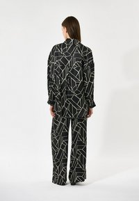 Sort mønstret skjorte og vide bukser med et geometrisk design i cremefarve. Glat stof med en afslappet pasform og knaplukning bagpå.