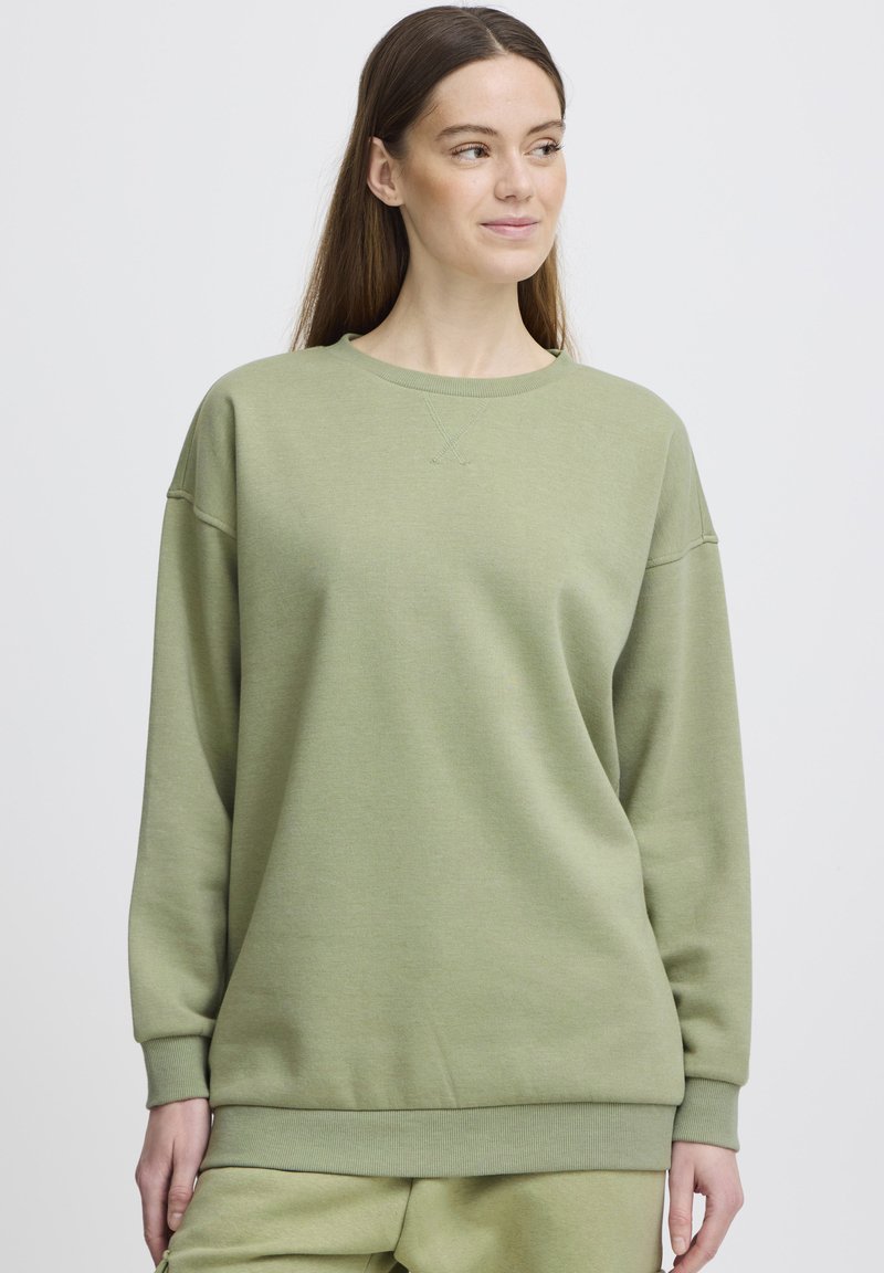 Felpa verde in morbido tessuto, con collo rotondo, spalle abbassate, polsini a coste e una vestibilità rilassata. Senza motivi né grafiche.