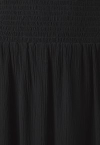 Robe noire avec corsage froncé smocké et jupe texturée et fluide. Tissu doux avec de légers plis verticaux sur toute la surface.