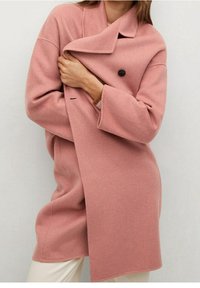 Lyserød uldblandingsfrakke med dobbeltradet design og brede klapper. Har knaplukning og afslappet pasform, vist over lyse bukser.