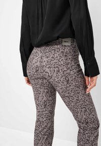 Grijze luipaardprint jeans met een aansluitend ontwerp, zachte textuur en achterzakken. Gecombineerd met een zwarte blouse met lange mouwen.