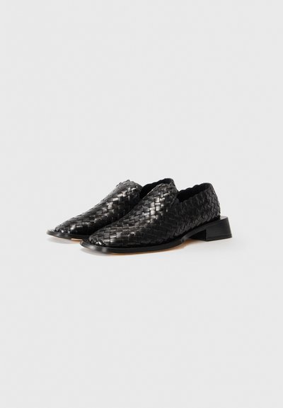 Par svarta läder vävda slip-on skor med låga klackar på en enkel vit bakgrund