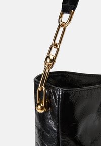 Bolso de mano negro hecho de material brillante, con una correa de cadena dorada con acentos redondos y un acabado texturizado. Diseño de apertura superior.