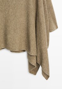 Châle en tricot beige avec une texture douce, présentant un design asymétrique et des bords fluides. Il tombe doucement, créant des plis délicats.