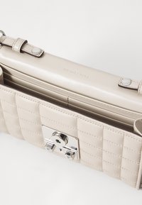 Borsa a tracolla in pelle trapuntata beige con una patta liscia e arrotondata. Presenta una chiusura in argento lucido e il nome del marchio impresso. Texture morbida evidente.