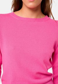 Pull en maille côtelée fuchsia avec encolure ronde et manches longues, présentant une texture douce et une coupe ajustée. Aucun motif ou accent notable.