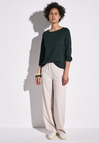 Haut en maille vert foncé à manches longues avec un col rond, associé à un pantalon large beige clair et des baskets blanches ; tissu texturé.