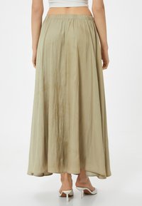 Falda maxi fluida de color beige con cinturilla elástica. La tela parece suave y semi-translúcida, con un ceñido suave y un brillo sutil.