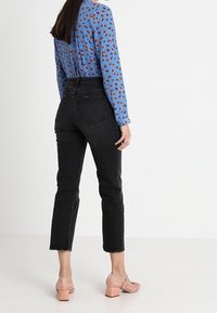 Blusa blu a maniche lunghe con motivo astratto marrone, abbinata a jeans neri a vita alta e scarpe con tacco a blocco rosa chiaro.