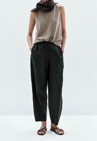 Hihaton ruskea paita, mustat naruhousut sivutaskuilla, yhdistettynä ruskeisiin sandaaleihin. Pehmeä kangas, rento istuvuus, minimaalinen muotoilu.