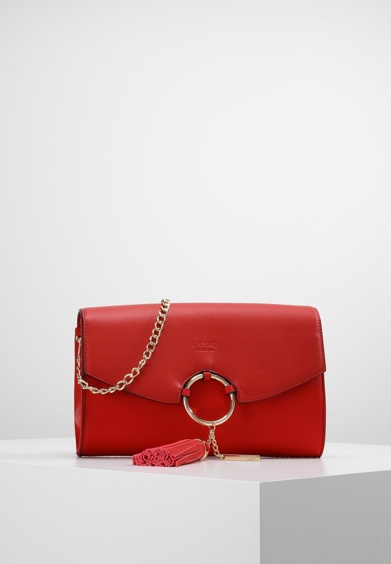 Borsa a mano in pelle rossa con patta pieghevole, tracolla in catena dorata, dettaglio in metallo circolare e pendente rosa.