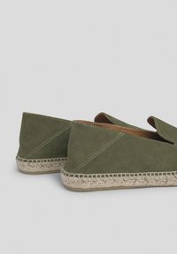 Espadrilles de ante verde con suela de yute, que presentan un diseño sin cierre y un detalle de costura exterior, abiertas en la parte frontal para ventilación.