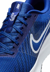 Niebieskie buty sportowe z teksturowanej siateczki, z białym logo Nike, ciemnoniebieskimi sznurówkami i białą, amortyzującą podeszwą.