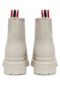 Beige ankle boots se hladkým syntetickým povrchem, s tlustou podrážkou a kontrastním červeným, černým a bílým poutkem na zadu.