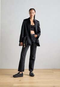 Blazer in pelle nera su un crop top nero, abbinato a jeans neri a vita alta e sneakers platform, con dettagli in hardware dorato.