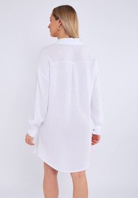 Robe chemise blanche à manches longues en tissu texturé, avec des poignets à boutons et un ourlet arrondi. Dotée d'un col classique et d'un détail de poignet au dos.