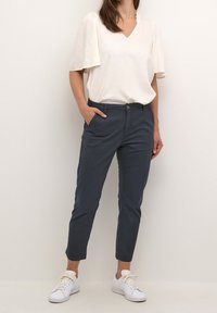 Ljus beige, kortärmad topp med V-ringning; marinblå slim-fit byxor; vita sneakers. Tyget verkar mjukt, med en avslappnad passform och rena linjer.