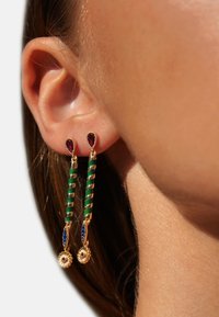 Boucles d'oreilles en or avec des tiges torsadées vertes et des accents de bijoux en rouge et bleu, présentant des détails floraux ronds aux extrémités.