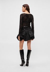 Top preto transparente de manga comprida com detalhes florais em lantejoulas, combinado com uma saia preta de cetim em estilo balão. Modelo usa botas pretas brilhantes até ao joelho.