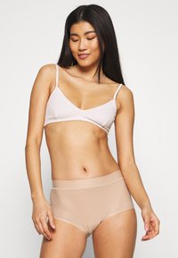 Bralet din căptușeală roz deschis, cu nervuri, și chiloți scurți fără cusături în nuanță nud. Ambele au texturi netede și modele simple, cu curele ajustabile și talie lată.