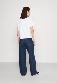 T-shirt branca de manga curta combinada com jeans de perna larga azul-escuro e ténis pretos, apresentando um ajuste casual e design minimalista.