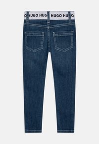 Tmavě modré džíny z denimu s bílým páskem, na kterém je značka "HUGO HUGO". Design s pěti kapsami a kontrastním prošíváním.