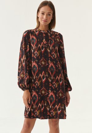 Long-sleeve, loose-fit dress in dark fabric with geometric and floral patterns in red, orange, and green. Features a high neckline and gathered sleeves.