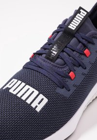 Námořnické modré sportovní tenisky vyrobené z prodyšné síťoviny, s bílým logem, červenými akcenty a texturovanými šňůrkami včetně poutka pro snadné obouvání.