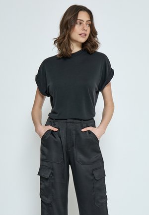 Top nero a maniche corte con colletto alto, abbinato a pantaloni cargo neri con tasche laterali e finitura testurizzata.