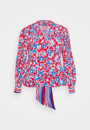 Blouse rouge à manches longues avec imprimé floral bleu et blanc, col en V, poignets rayés et détail de nœud rayé rouge, blanc et bleu à la taille.