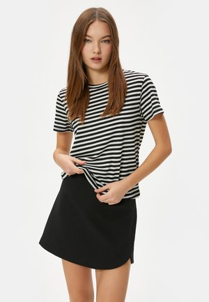 Camiseta de rayas en blanco y negro con mangas cortas, combinada con una falda negra con dobladillo curvado y aberturas laterales.