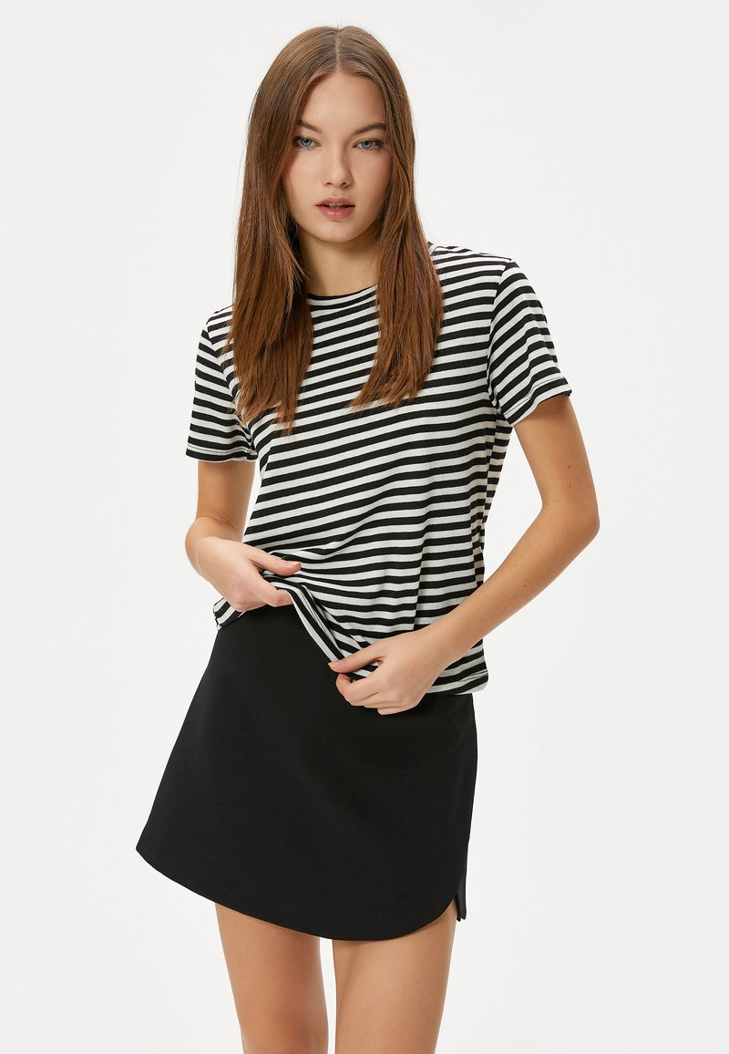 Camiseta de rayas en blanco y negro con mangas cortas, combinada con una falda negra con dobladillo curvado y aberturas laterales.