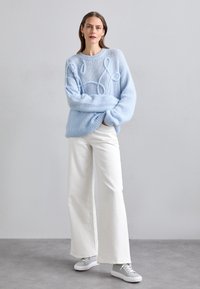 Maglione lavorato a maglia azzurro chiaro con dettagli in rilievo e orlo a coste, abbinato a pantaloni bianchi a gamba larga e sneakers grigio chiaro.